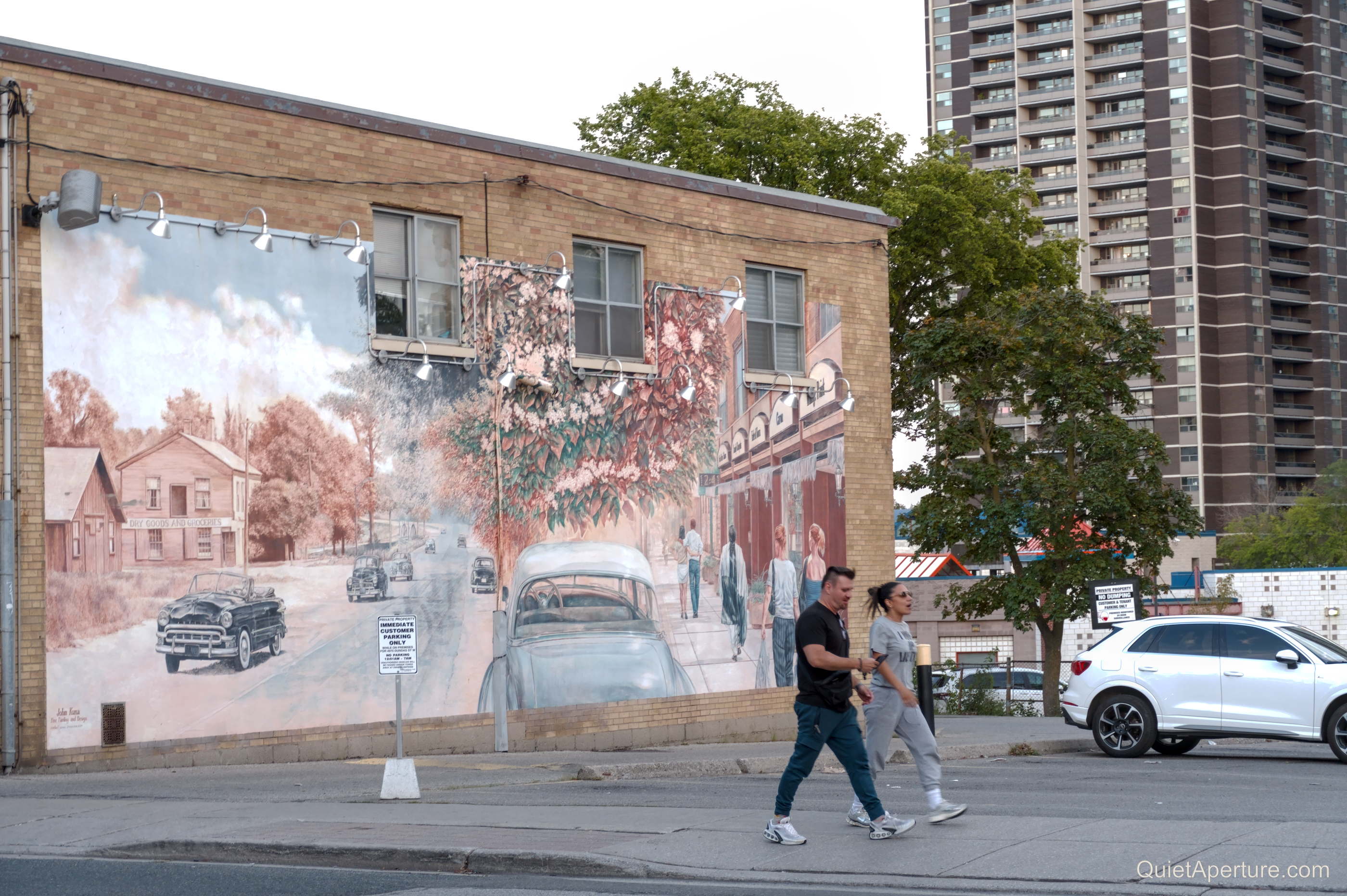 A sepia-toned neighbourhood street mural on a brick wall, frame 04.